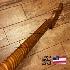 Puede incluir: Un m&aacute;stil de guitarra de madera marr&oacute;n claro con un patr&oacute;n de veta de arce flameado con rayas de tigre. El clavijero presenta varios orificios pretaladrados para las clavijas. El texto Guitar_Closet eBay es visible en la madera.