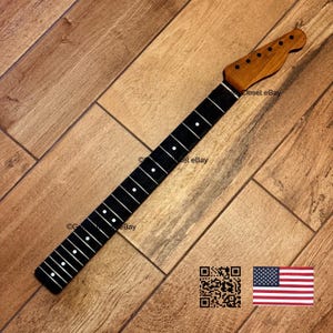May include: A guitar neck with a dark fretboard and a light brown headstock. The fretboard has white dot inlays. The headstock has pre-drilled holes for tuning pegs. The image includes a QR code and the American flag.