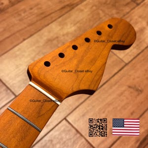 Puede incluir: Un clavijero de guitarra de madera marr&oacute;n claro con seis orificios circulares para las clavijas, una cejuela blanca y veta de madera visible. El texto Guitar_Closet eBay est&aacute; impreso en la superficie. Un c&oacute;digo QR y una bandera de EE. UU. son visibles.