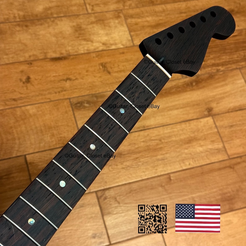 Peut inclure: Un manche de guitare brun fonc&eacute; avec des rep&egrave;res de frettes blancs et une t&ecirc;te avec des trous pour les chevilles d'accord. Le manche a une finition lisse et est pos&eacute; sur un fond en bois. L'image comprend un code QR et le drapeau am&eacute;ricain.