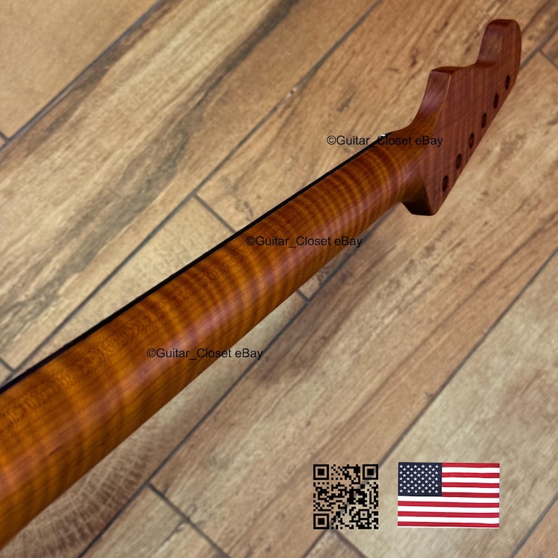 May include: A close-up of a guitar neck made of figured wood, showcasing a rich, reddish-brown hue with prominent grain patterns. The headstock features tuning peg holes. The image includes a QR code and a US flag.