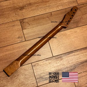May include: A wooden guitar neck with a natural finish. The neck has a headstock with six tuning peg holes and a smooth, curved profile. The wood grain is visible, and the neck appears to be new. The image includes a QR code and an American flag.