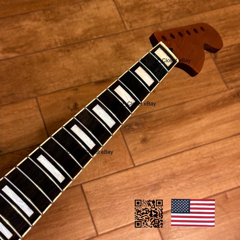 May include: A guitar neck with a dark wood fretboard and a lighter wood headstock. The fretboard has white rectangular inlays. The headstock has tuning peg holes. The background is a wooden surface.