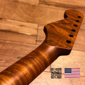 May include: A guitar neck with a natural wood grain finish and a headstock featuring six tuner holes. The wood displays a distinct wavy pattern throughout the length of the neck. The text Guitar_Closet eBay appears on the surface.
