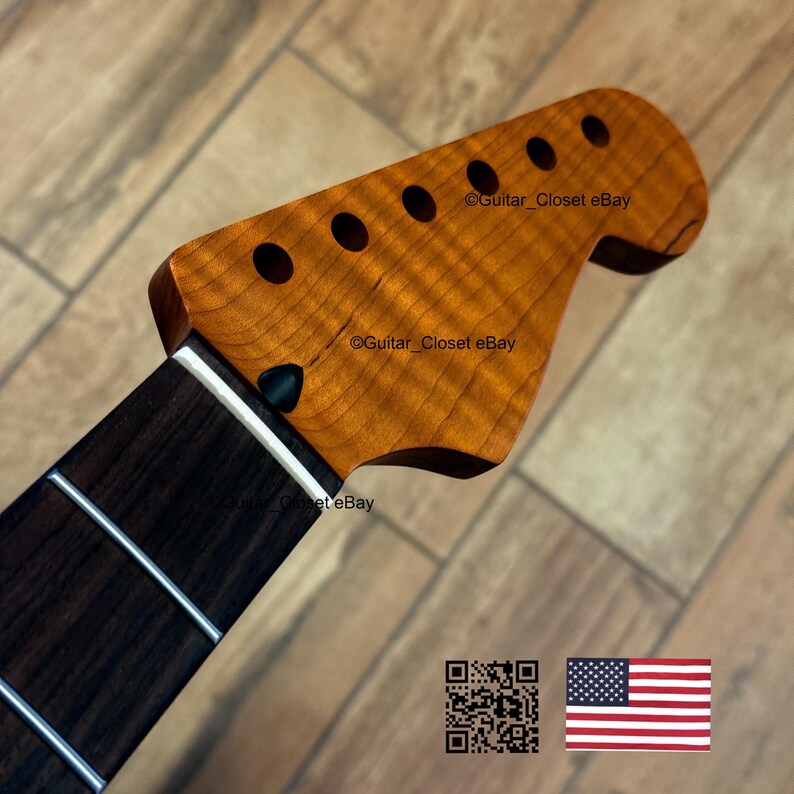 May include: Close-up of a guitar neck and headstock. The headstock is a light brown color with six circular holes and the text "Guitar_Closet eBay". The neck is dark brown with silver frets. An American flag is in the bottom right corner.