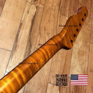 May include: A close-up of a guitar neck with a flamed maple finish. The wood grain has a wavy pattern with shades of amber and brown. The headstock has six tuning peg holes. The image includes a QR code and the American flag.