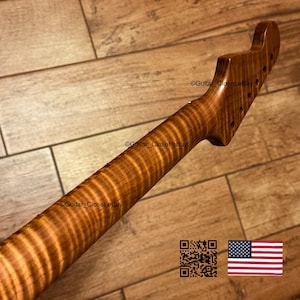 Puede incluir: Un m&aacute;stil de guitarra hecho de madera marr&oacute;n claro con un patr&oacute;n de veta de arce flameado con rayas de tigre. El clavijero presenta seis orificios pretaladrados para las clavijas. La superficie tiene un acabado liso y pulido con texturas naturales.