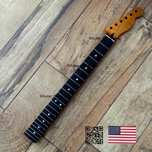 以下が含まれることがあります： 自然な木材仕上げのヘッドストックと、白いドットインレイが付いた黒い指板を備えたギターネック。 ネックは木製の表面に角度が付けられています。 画像にはQRコードと小さなアメリカ国旗が含まれています。