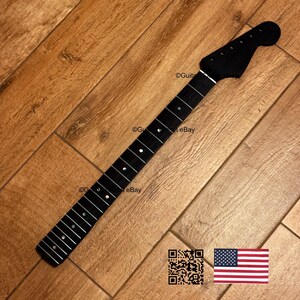 Peut inclure: Un manche de guitare noir avec des rep&egrave;res de frettes blancs. Le manche est en bois fonc&eacute; et poss&egrave;de une t&ecirc;te avec des trous pour les chevilles d'accord. L'image comprend un code QR et un drapeau am&eacute;ricain.