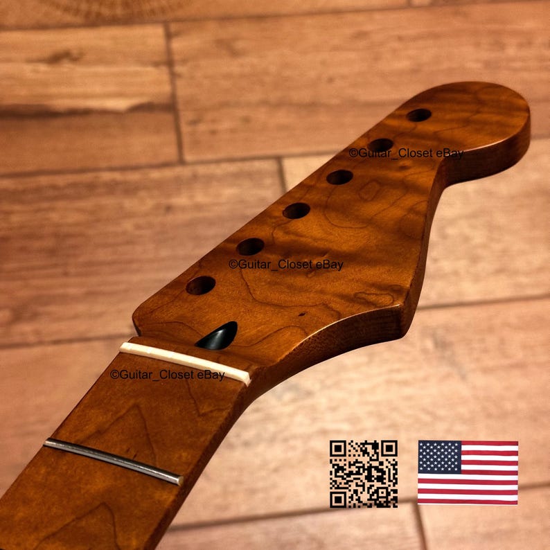 May include: A guitar neck with a natural wood grain finish, featuring a headstock with six tuner holes, a white nut, and a single metal fret visible. The wood has a warm, medium-brown tone with visible grain patterns throughout the surface.