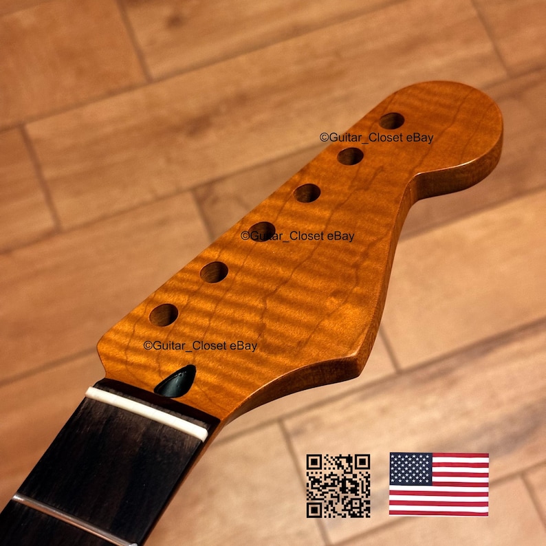 May include: A guitar neck with a flamed maple headstock and a dark fretboard. The headstock has six tuning peg holes and a natural finish. The neck is angled and has a white stripe at the base. The American flag is in the bottom right corner.