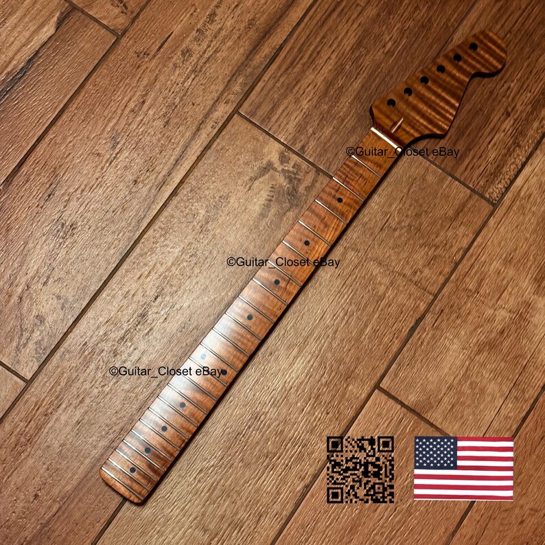 May include: A guitar neck featuring a flamed maple wood grain pattern with a natural brown finish. The neck includes a fretboard with dark circular fret markers and silver frets. The headstock has six pre-drilled holes for tuning pegs.