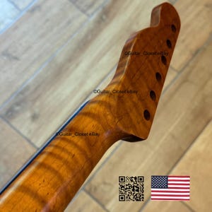 May include: A close-up of a guitar neck and headstock, showcasing a warm, amber-toned wood grain. The headstock features six tuning peg holes. The neck has a dark blue stripe. The image includes the text "Guitar Closet eBay" and a QR code with the American flag.