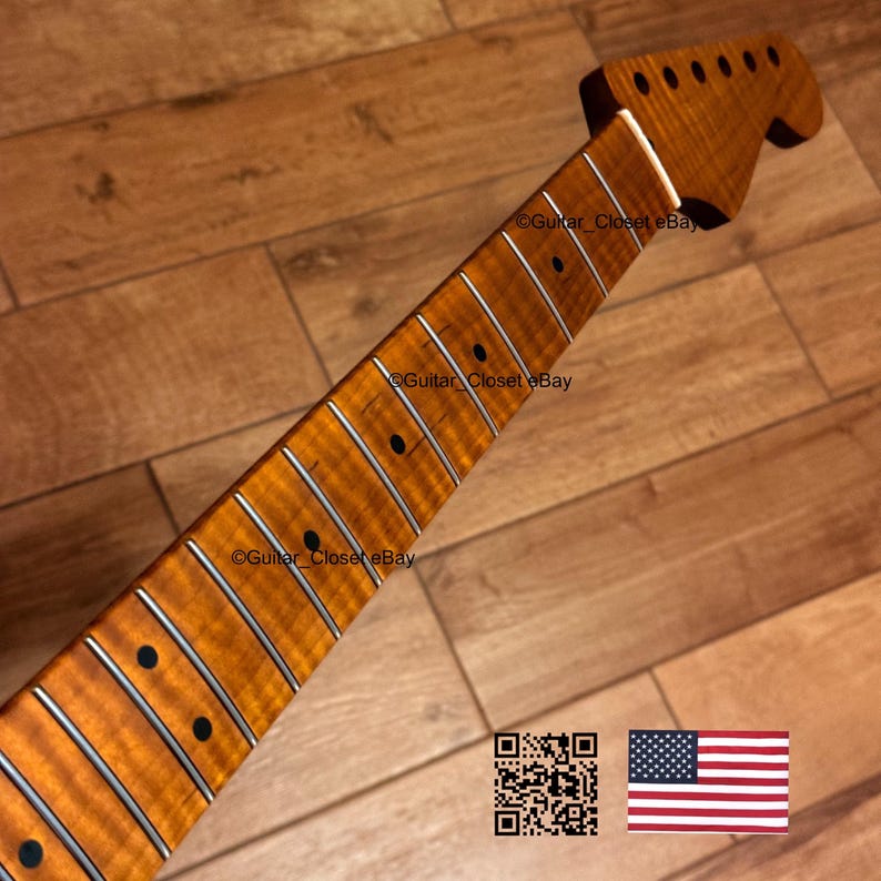 May include: A guitar neck with a flamed maple finish. The neck has a headstock with tuning peg holes and a fretboard with inlaid frets and black dot markers. The wood grain is visible, and the finish is a warm amber colour.