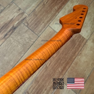 May include: Close-up of a guitar neck with a natural wood finish. The neck has a headstock with tuning peg holes. The wood grain is visible, with a wavy pattern. The text "Guitar Closet eBay" is visible on the neck.