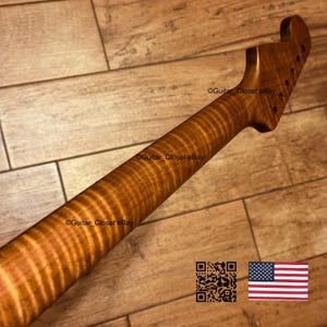 Puede incluir: Un m&aacute;stil de guitarra fabricado en madera de arce flameado de tono &aacute;mbar, con un patr&oacute;n de veta distintivo en rayas de tigre. El clavijero est&aacute; inclinado con orificios pretaladrados para las clavijas, mostrando la textura natural.
