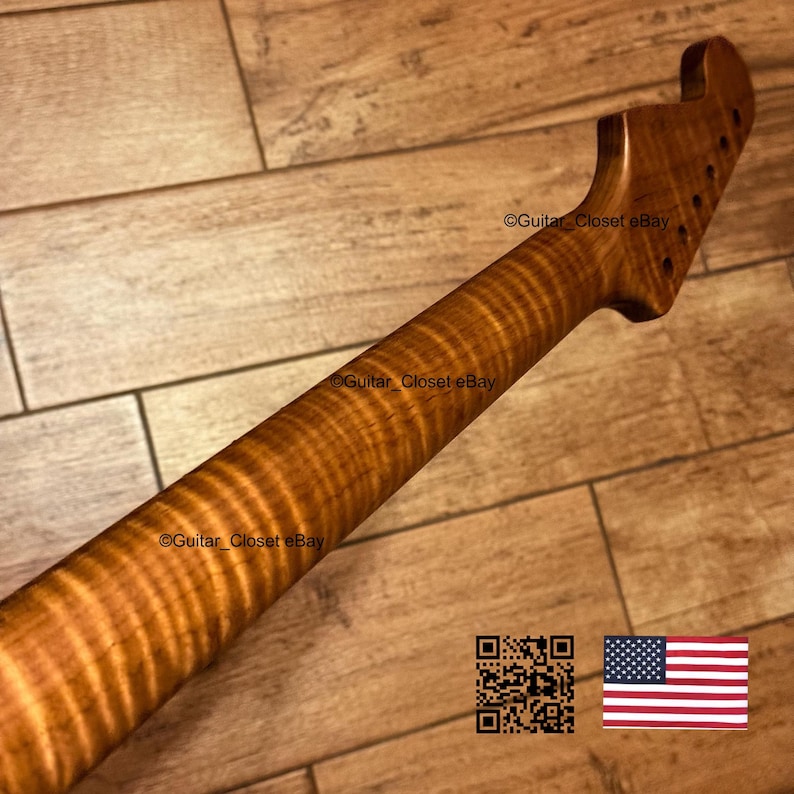 Puede incluir: Un m&aacute;stil de guitarra fabricado en madera de arce flameado de tono &aacute;mbar, con un patr&oacute;n de veta distintivo en rayas de tigre. El clavijero est&aacute; inclinado con orificios pretaladrados para las clavijas, mostrando la textura natural.
