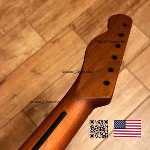 K&ouml;nnte beinhalten: Gitarrenhals aus Holz mit nat&uuml;rlicher Oberfl&auml;che, mit L&ouml;chern f&uuml;r die Stimmwirbel und einem schwarzen Streifen. Die Kopfplatte hat eine klassische Form. Das Bild enth&auml;lt einen QR-Code und die amerikanische Flagge.