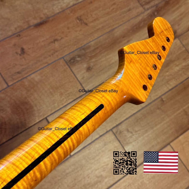 May include: A close-up of a guitar neck with a flamed maple finish. The neck has a dark stripe down the center and six tuning peg holes. The headstock is shaped with a rounded top. The wood grain is visible.