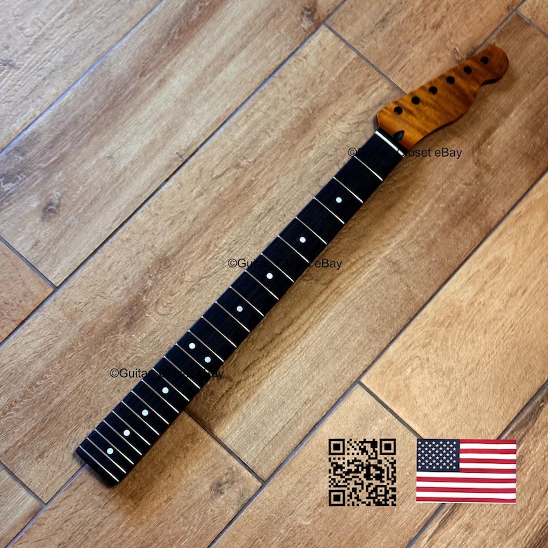 May include: A guitar neck with a dark fretboard and white dot inlays. The headstock is a lighter wood with a flamed grain pattern. The neck is angled on a wooden surface. A QR code and American flag are in the lower right corner.