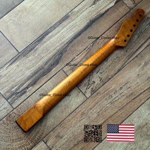 以下が含まれることがあります： 6つのチューニングペグ穴があるヘッドストックを備えた、明るい茶色のギターネック。 ネックは木製で、滑らかで磨かれた仕上がりです。 画像にはQRコードと小さなアメリカ国旗が含まれています。