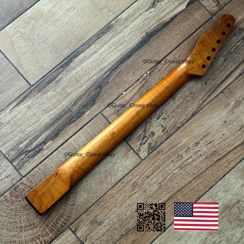 以下が含まれることがあります： 6つのチューニングペグ穴があるヘッドストックを備えた、明るい茶色のギターネック。 ネックは木製で、滑らかで磨かれた仕上がりです。 画像にはQRコードと小さなアメリカ国旗が含まれています。