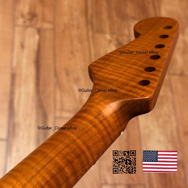 May include: Close-up of a guitar neck with a flamed maple finish. The neck has six tuning peg holes and a smooth, polished surface. The wood grain is visible, with a warm, amber color. The text "Guitar_Closet eBay" is visible.