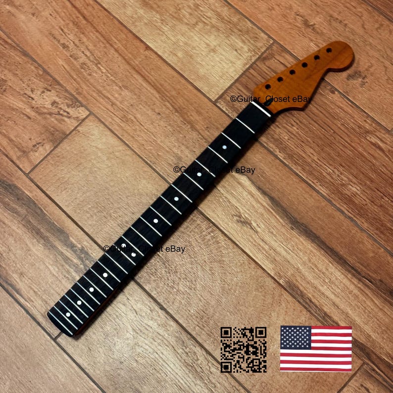 May include: A guitar neck with a brown headstock and a black fretboard with white inlays. The neck is angled on a wooden surface. The American flag and a QR code are in the bottom right corner.