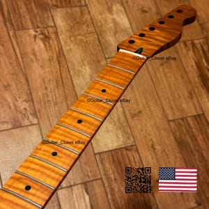 May include: A guitar neck with a flamed maple finish. The neck has a light brown color with dark brown fret markers and silver frets. The headstock has tuning peg holes. The text "Guitar Closet eBay" is visible on the neck.
