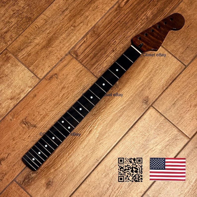 May include: A guitar neck with a dark brown headstock and a black fretboard with white dot inlays. The neck is angled on a wooden surface. The image includes a QR code and an American flag.