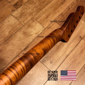 May include: A guitar neck crafted from figured wood, displaying a swirling grain pattern in shades of brown and amber. The headstock features pre-drilled holes for tuning pegs. The image includes a QR code and the American flag.