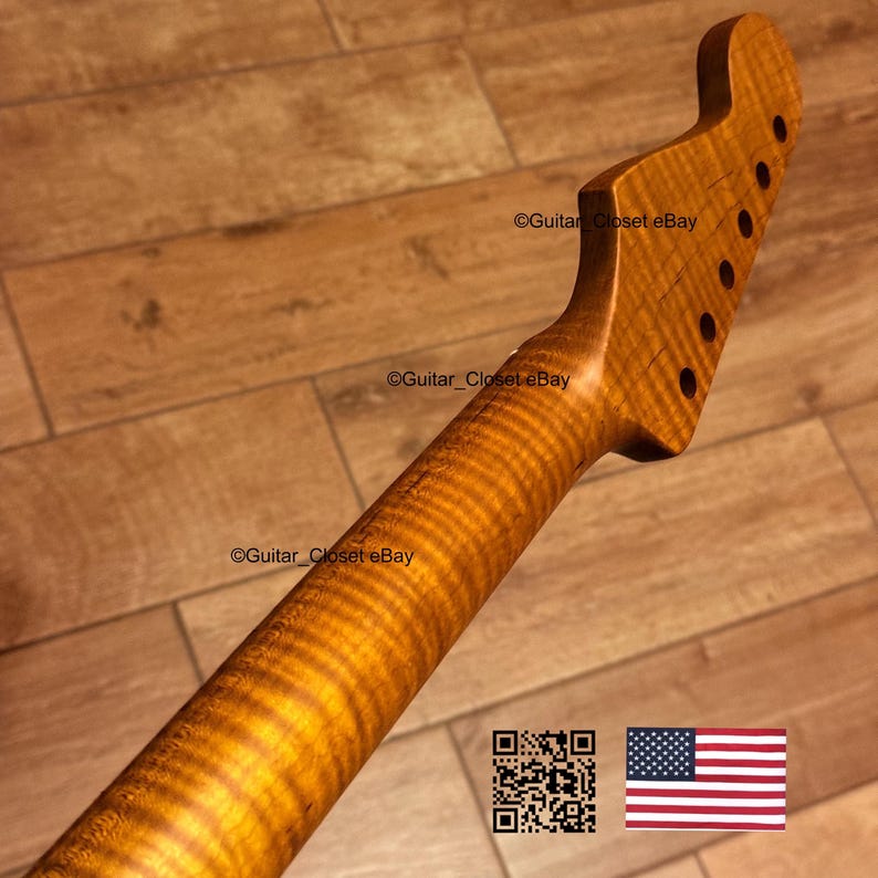 May include: A guitar neck with a flamed maple finish, showing a distinctive wavy wood grain pattern. The headstock features six tuning peg holes. The background is a wooden surface. The American flag is in the bottom right corner.