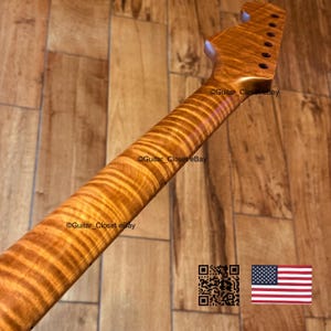 May include: A guitar neck with a flamed maple finish. The neck has a natural wood grain pattern and is angled towards the top of the image. The headstock has tuning peg holes. The text "Guitar Closet eBay" is visible on the neck.