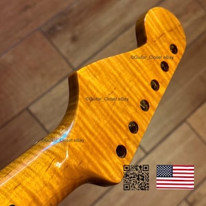 May include: Close-up of a guitar neck with a flamed maple finish. The wood grain has a wavy pattern with a golden-yellow hue. There are six tuning peg holes. The text "Guitar_Closet eBay" is visible. An American flag and a QR code are in the image.