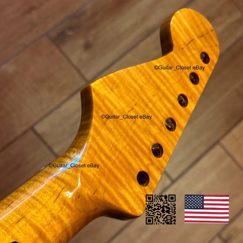 May include: Close-up of a guitar neck with a flamed maple finish. The wood grain has a wavy pattern with a golden-yellow hue. There are six tuning peg holes. The text "Guitar_Closet eBay" is visible. An American flag and a QR code are in the image.