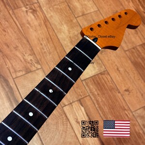 May include: A guitar neck with a natural wood finish. The headstock has six tuning peg holes. The fretboard is dark brown with white dot inlays. The text "Guitar Closet eBay" is visible. An American flag is in the bottom right corner.