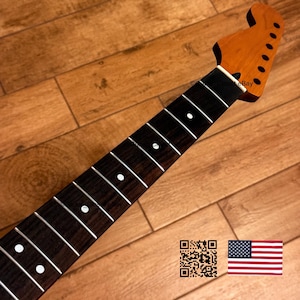 K&ouml;nnte beinhalten: Ein Gitarrenhals mit einer braunen Kopfplatte und einem dunkelbraunen Griffbrett. Das Griffbrett hat wei&szlig;e Einlagen und B&uuml;nde. Der Hals ist zur oberen rechten Ecke abgewinkelt. Der Hintergrund ist eine Holzoberfl&auml;che.
