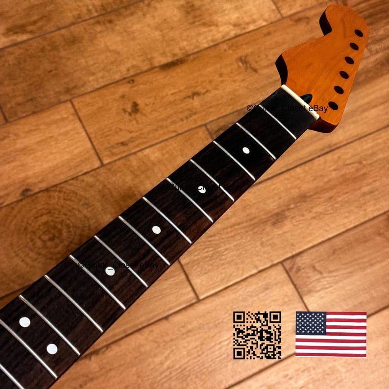K&ouml;nnte beinhalten: Ein Gitarrenhals mit einer braunen Kopfplatte und einem dunkelbraunen Griffbrett. Das Griffbrett hat wei&szlig;e Einlagen und B&uuml;nde. Der Hals ist zur oberen rechten Ecke abgewinkelt. Der Hintergrund ist eine Holzoberfl&auml;che.