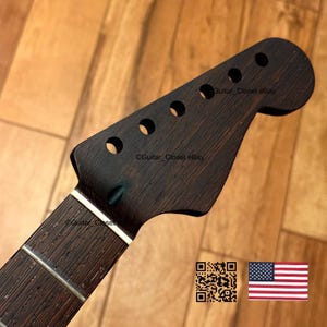 May include: A dark brown, wood-grain guitar headstock featuring six tuner holes, a smooth finish, and a visible nut. The surface displays a natural, deep-toned timber texture with distinct grain patterns throughout the entire headstock component.