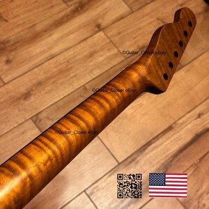 May include: A guitar neck with a flamed maple finish. The neck has a natural wood grain pattern and is a warm brown color. The headstock has six tuning peg holes. The image includes a QR code and the American flag.