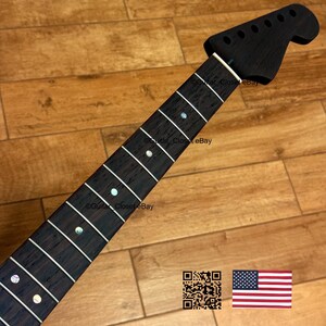 Peut inclure: Un manche de guitare teint&eacute; fonc&eacute; avec des rep&egrave;res de frettes blancs et une t&ecirc;te avec des trous de chevilles. Le manche a une finition lisse et polie. L'image comprend un code QR et le drapeau am&eacute;ricain.