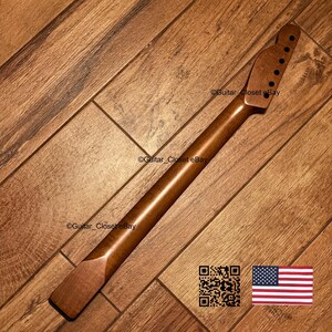 May include: A smooth, medium-brown wooden guitar neck featuring a headstock with six pre-drilled tuning peg holes. The neck has a natural wood grain finish and a flat heel base, designed for attachment to a guitar body. The surface is polished.