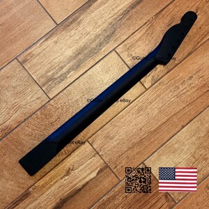 May include: A black guitar neck with a headstock, ready for assembly. The neck is made of wood and has a smooth, dark finish. The image is set against a wooden background.