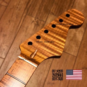 May include: A guitar headstock crafted from amber-toned flamed maple wood featuring a distinct wavy grain pattern, six tuner holes, and a white nut. The surface displays the text Guitar_Closet eBay, a QR code, and a small United States flag icon.