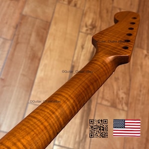 May include: A close-up of a guitar neck made of figured maple wood. The neck has a warm, amber color with a prominent wood grain pattern. The headstock features tuning peg holes. The text "Guitar_Closet eBay" is visible.