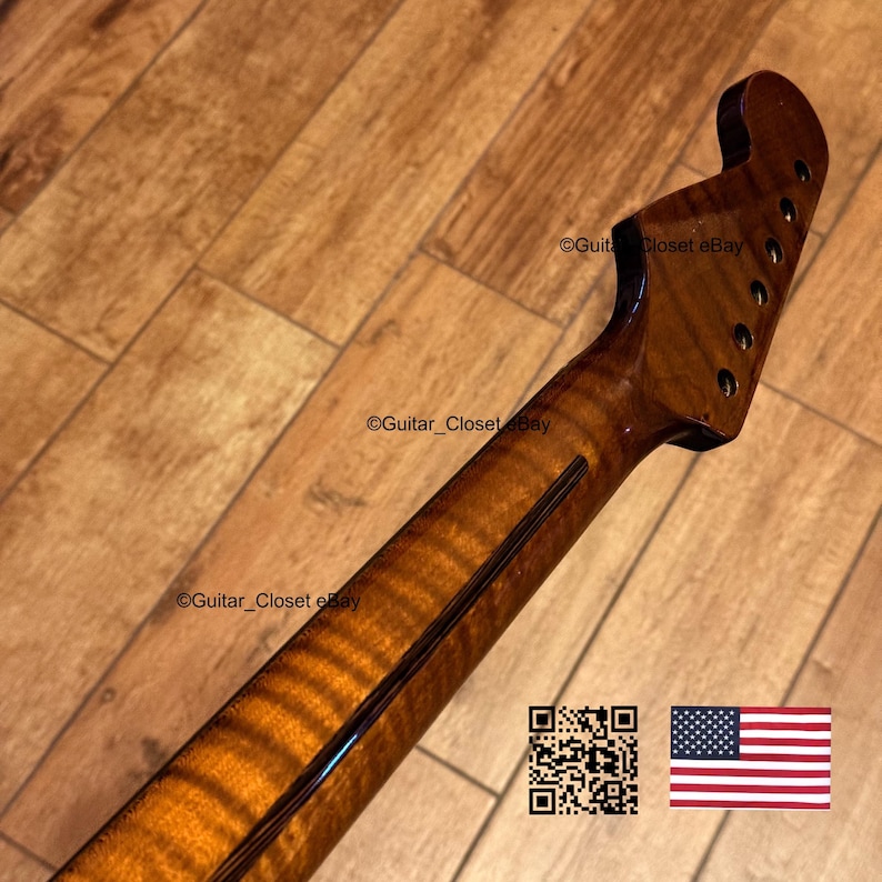 May include: A close-up of a guitar neck with a dark, glossy finish. The wood grain is visible, with a striped pattern. The headstock has tuning peg holes. The image includes a QR code and the American flag.