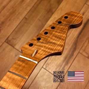 K&ouml;nnte beinhalten: Ein Gitarrenhals mit einer Kopfplatte aus geflammtem Ahorn in nat&uuml;rlichem Bernsteinton, sechs Mechanikbohrungen, einem wei&szlig;en Sattel und einem Griffbrett mit sichtbaren Metallb&uuml;nden. Die Holzmaserung zeigt ein deutliches Wellenmuster.