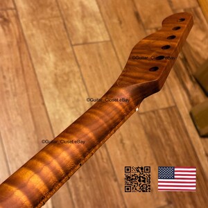 May include: A guitar neck made of figured wood, featuring a natural wood grain pattern. The headstock has six tuning peg holes. The neck is a warm brown color with a glossy finish. The image includes a QR code and the American flag.