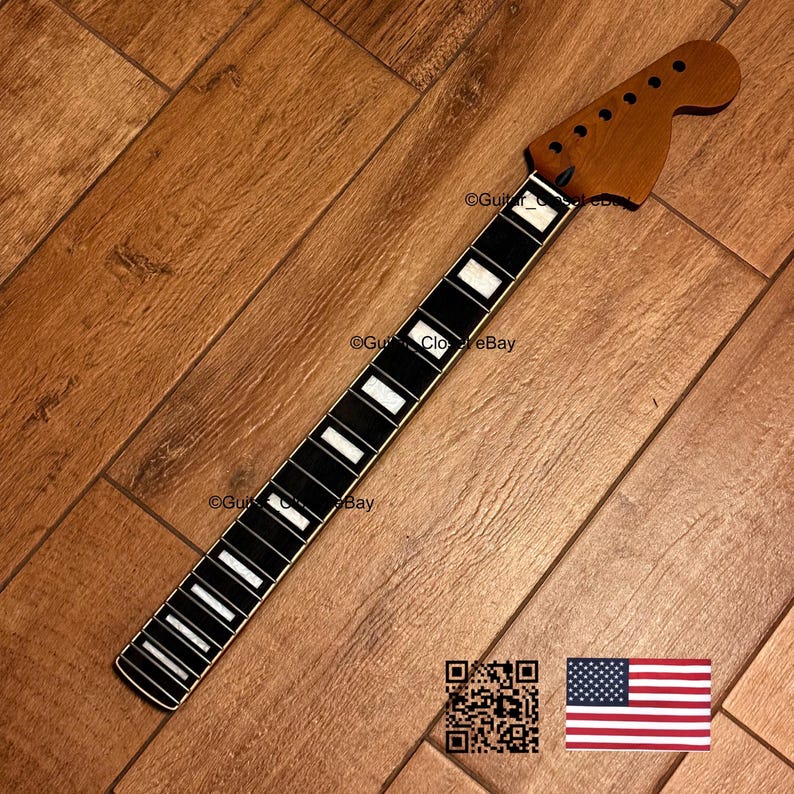 May include: A guitar neck with a dark brown headstock and a black fretboard with white inlays. The neck is set against a wooden background. The image includes a QR code and a small American flag.