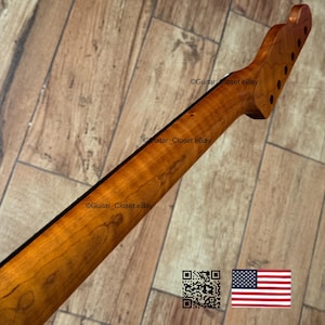 以下が含まれることがあります： 自然な木材仕上げのギターネック。ペグ穴のあるヘッドストックが特徴です。ネックの背面には濃いストライプがあり、明るい茶色です。画像にはQRコードとアメリカ国旗が含まれています。